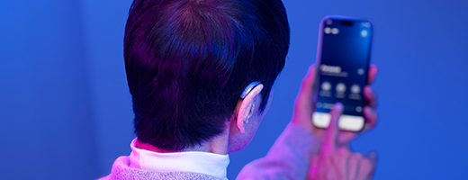 Image of woman wearing standard hearing aid and using the My Starkey app on her smartphone